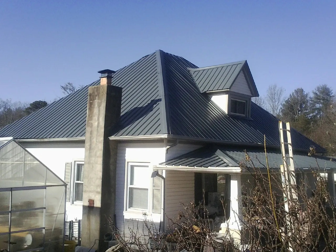 Dark blue standing seam metal roof on a white farmhouse with dormer — Slate & Tile Roof Repair by Roofing Brothers in Mesquite