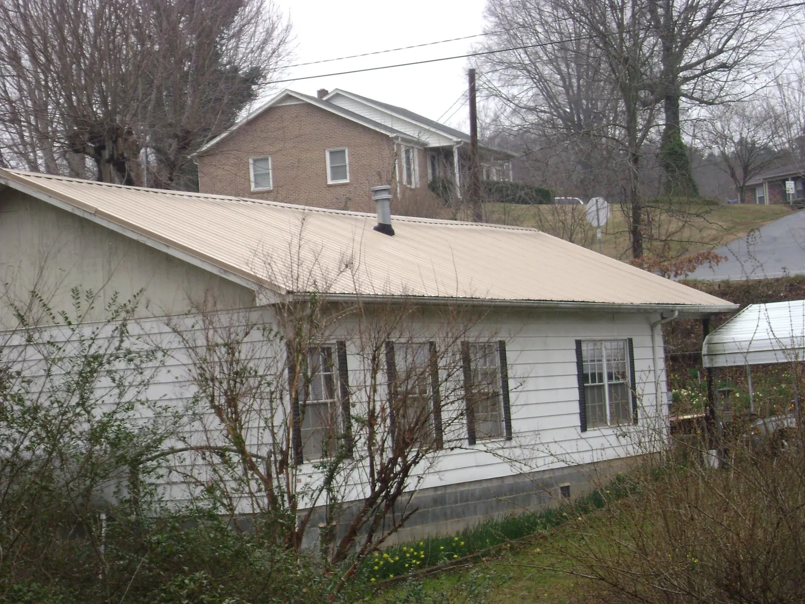 Tan metal roof on a white sided house set into a hillside — Commercial Roofing by Roofing Brothers in Mesquite